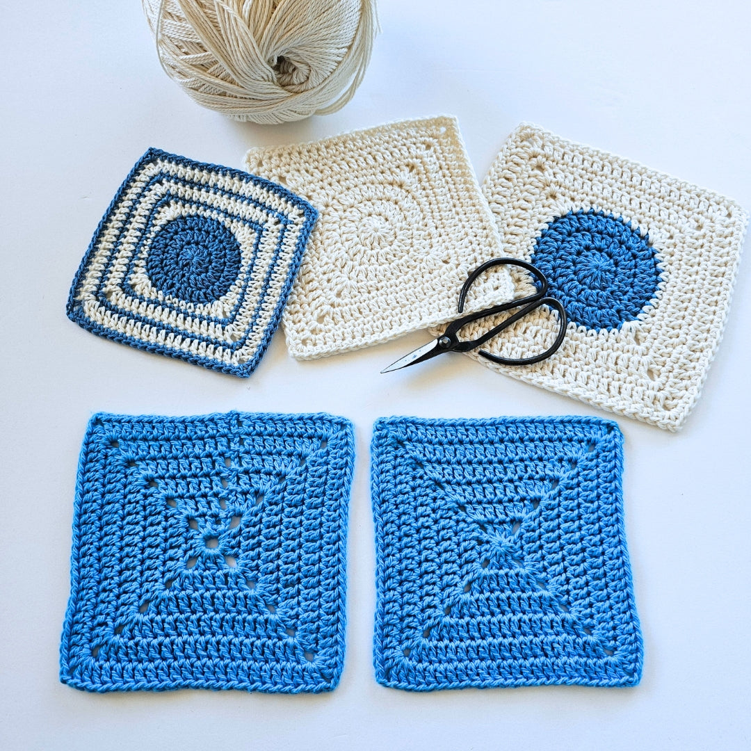 Crocheted squares in blue and white with a ball of yarn and scissors on a light background