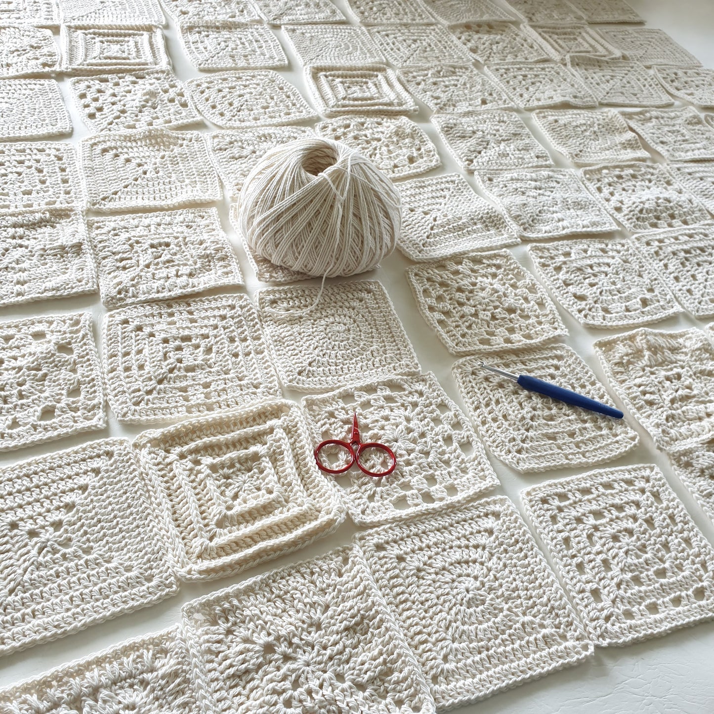 Granny squares from Granny Square Academy book by Shelley Husband with a ball of yarn, a blue handled silver crochet hook and a tiny pair of red yarn scissors