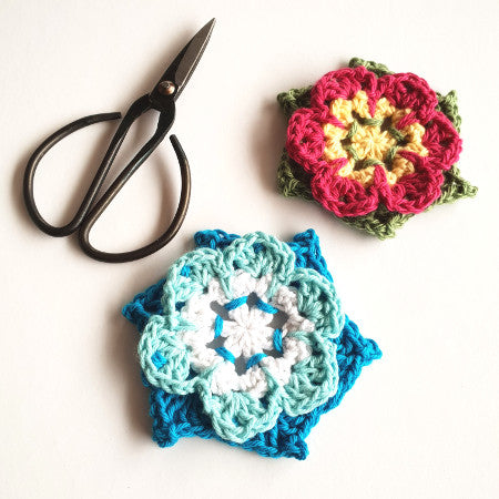 Two crochet flowers in different colours from Pinwheel Flower Pattern by Shelley Husband with a pair of black yarn scissors