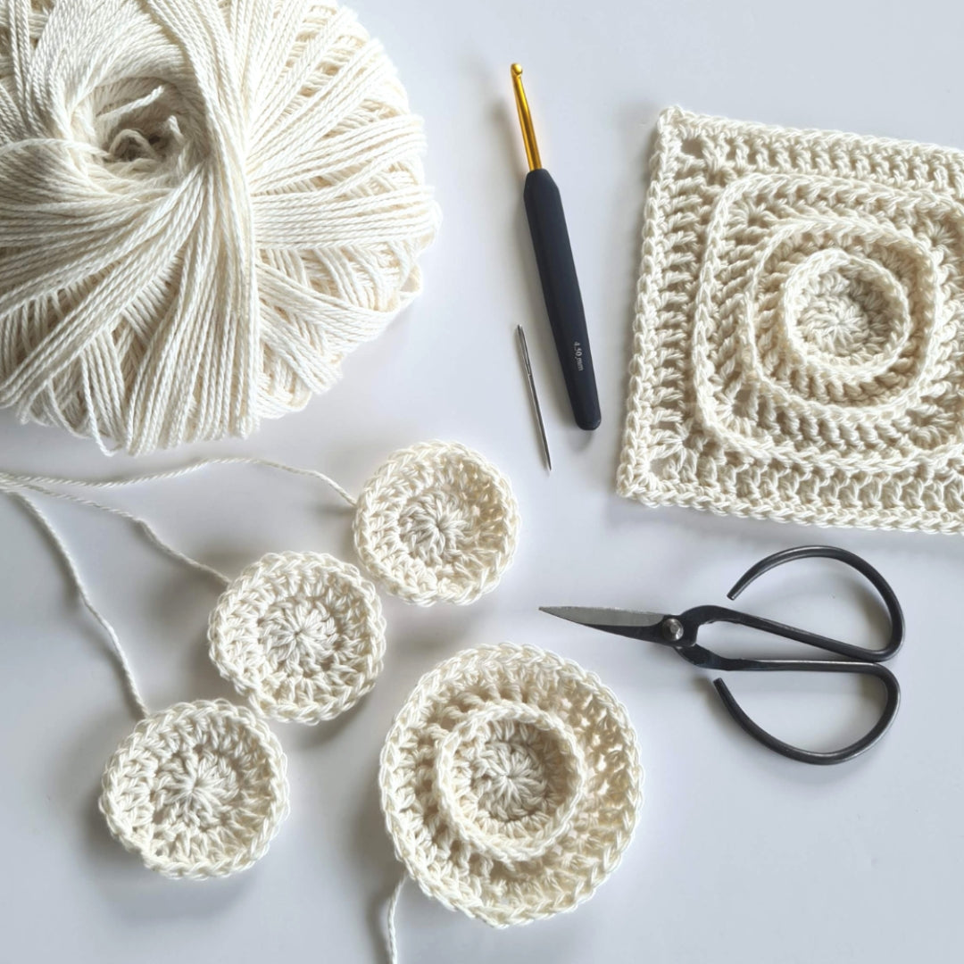 Crocheted squares and circular patterns with yarn, crochet hook, and scissors on a light background