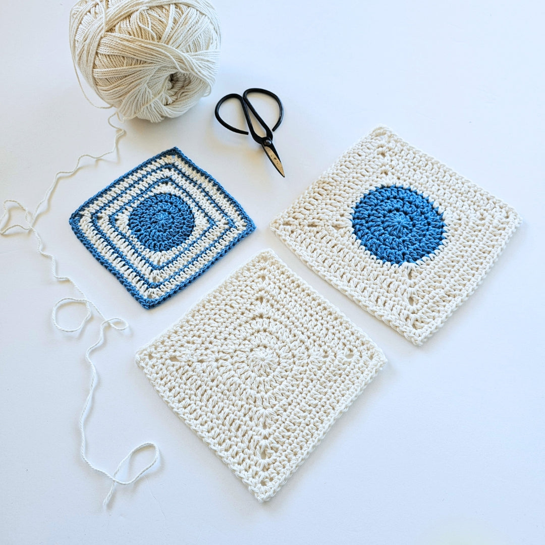 Three crocheted squares with blue centers on a white background, accompanied by yarn and scissors.