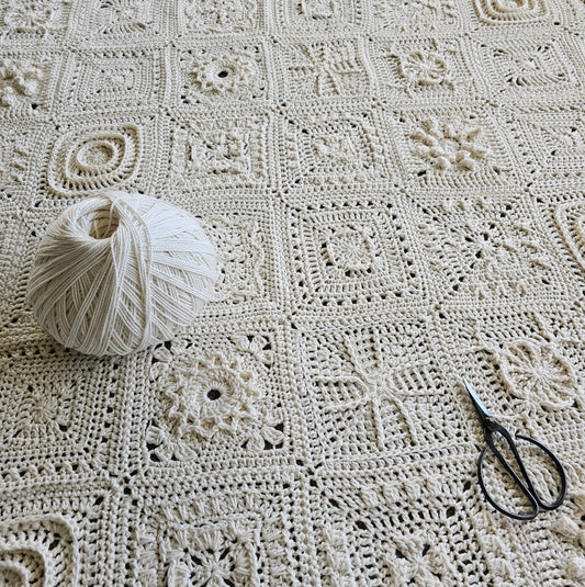 Granny Square Academy 2 sampler blanket in parchment with a ball of parchment yarn on top with a pair of black yarn scissors