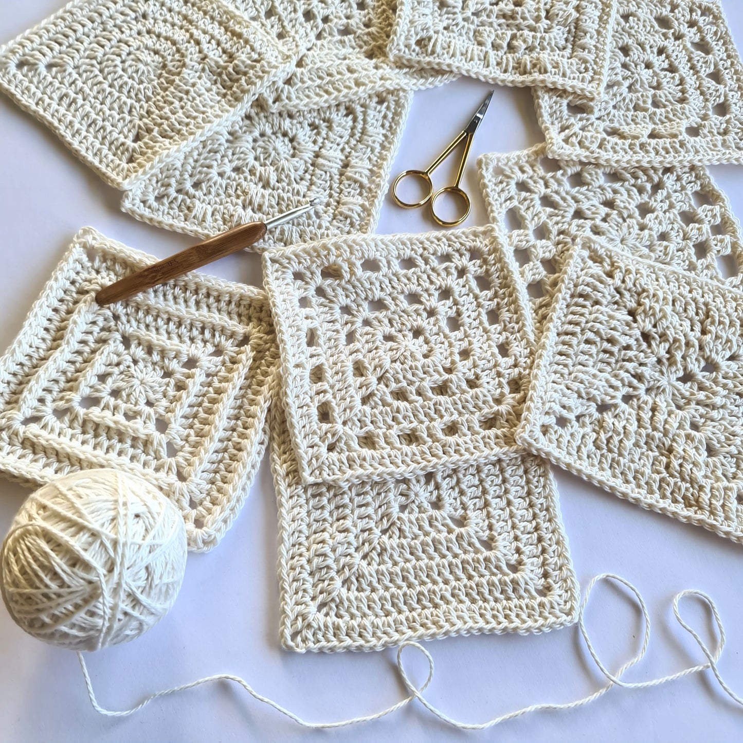 Granny squares from Granny Square academy with a wood handled silver crochet hook, gold yarn scissors and a ball of yarn