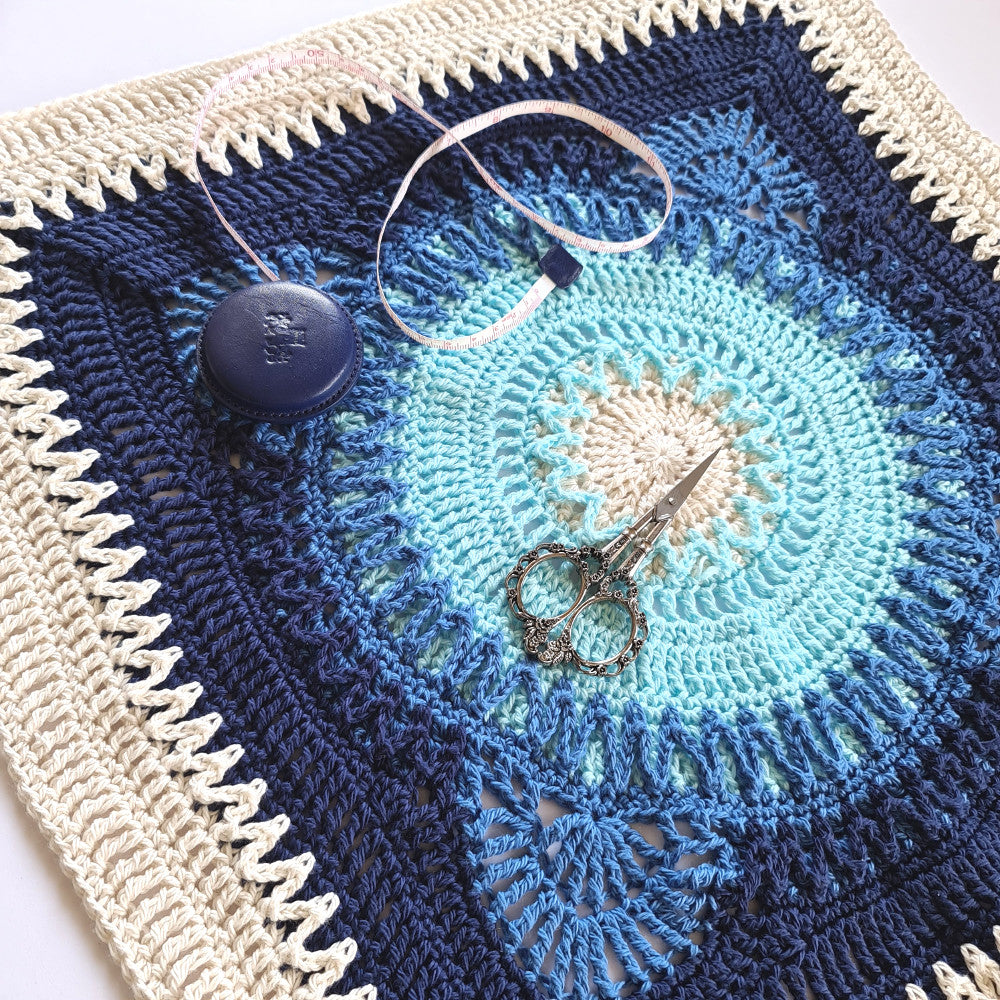 Hope large granny square in blues and white with a retractable tape measure and an ornate pair of yarn scissors by Shelley Husband