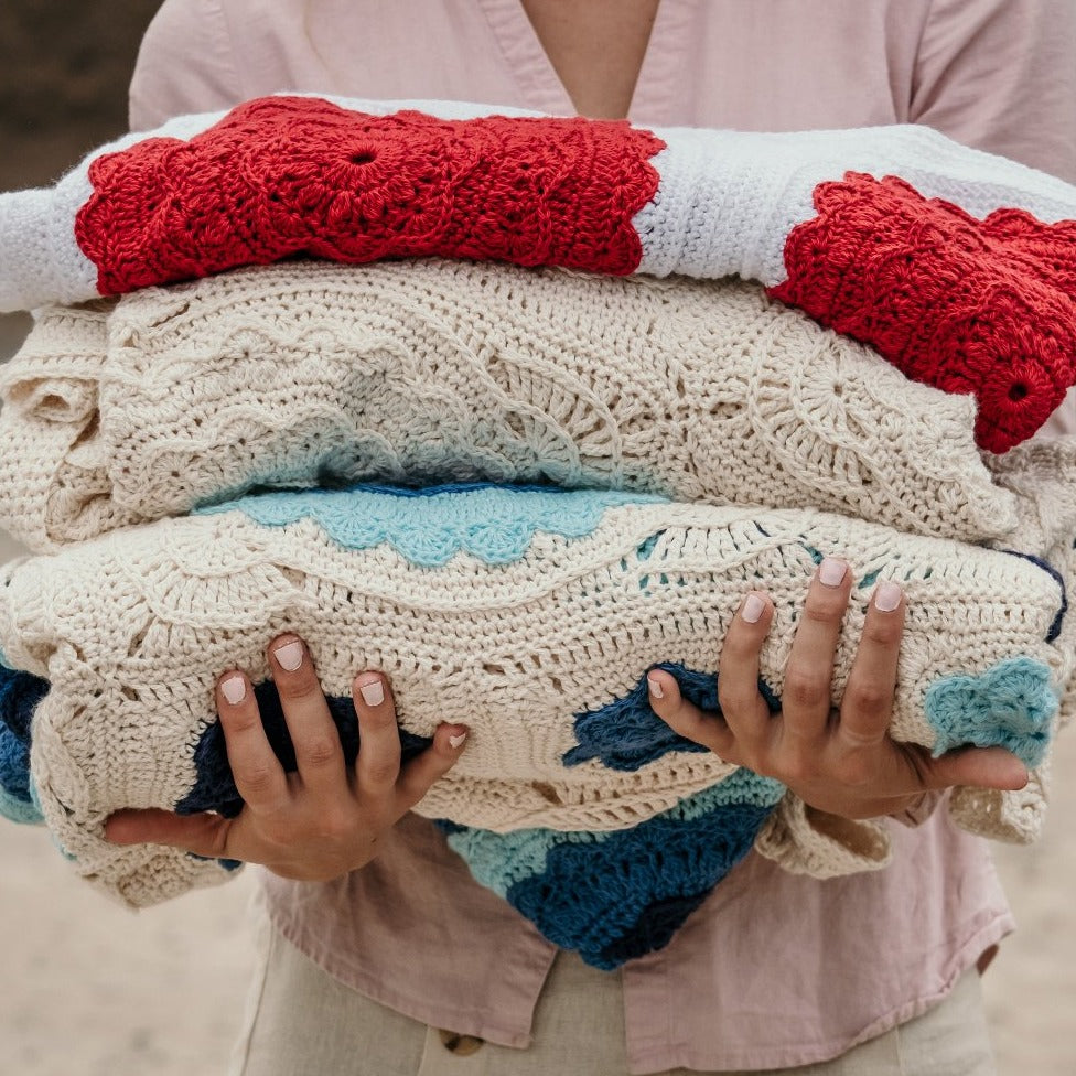 Three Manderley Crochet Blankets by Shelley Husband in different colours being held with two hands