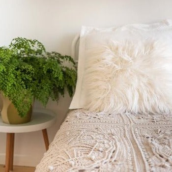 Light grey Mayan Crochet Blanket Pattern by Shelley Husband on a bed with white cushions and a plant on the sidetable