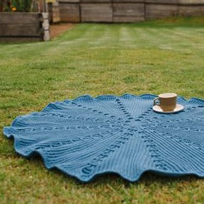 Millpond blanket by Shelley Husband laid over grass with a cup of tea on top