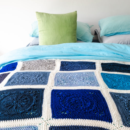 Oceanic crochet blanket on bed with green cushion and blue pillows