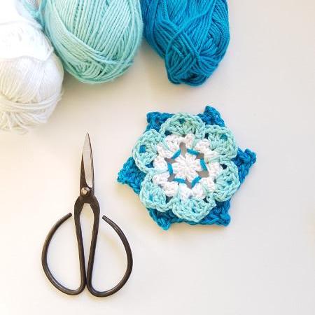 Light blue mid blue and white Pinwheel Flower Pattern by Shelley Husband with three balls of yarn and a pair of black yarn scissors