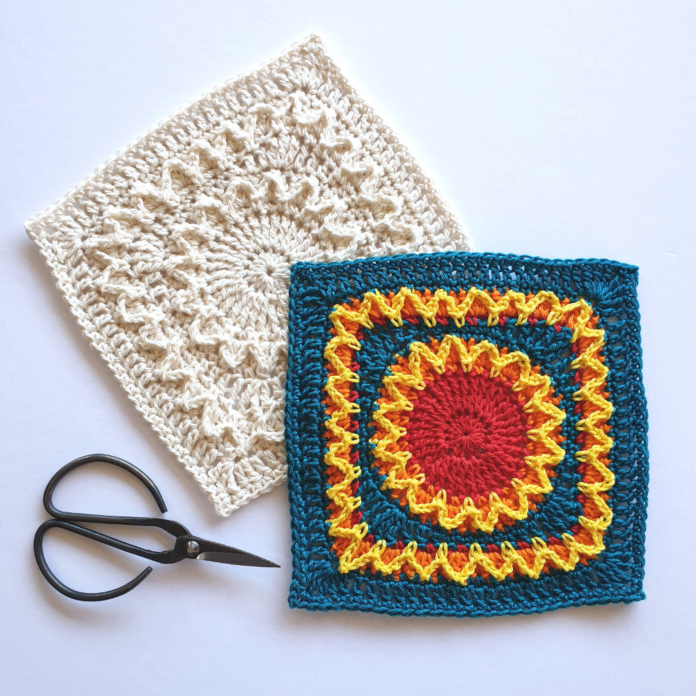 Two Shine with Hope Granny Squares in different colours and a pair of black yarn scissors by Shelley Husband