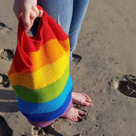 Close up of Spectrum Project Bag by Shelley Husband being held by the handles on the beach