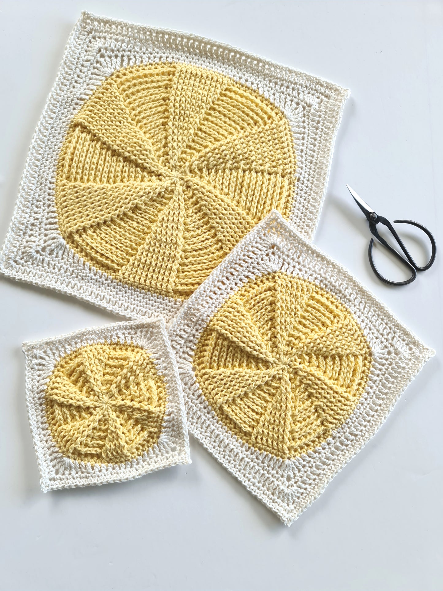 Three different size cream and yellow Vinyl Revival Granny square crochet patterns by Shelley Husband with a pair of black yarn scissors