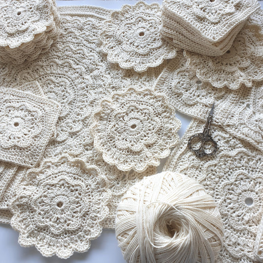 Granny squares and floral pieces from Manderley Crochet Blanket by Shelley Husband with a ball of parchment yarn and a pair of ornate yarn scissors