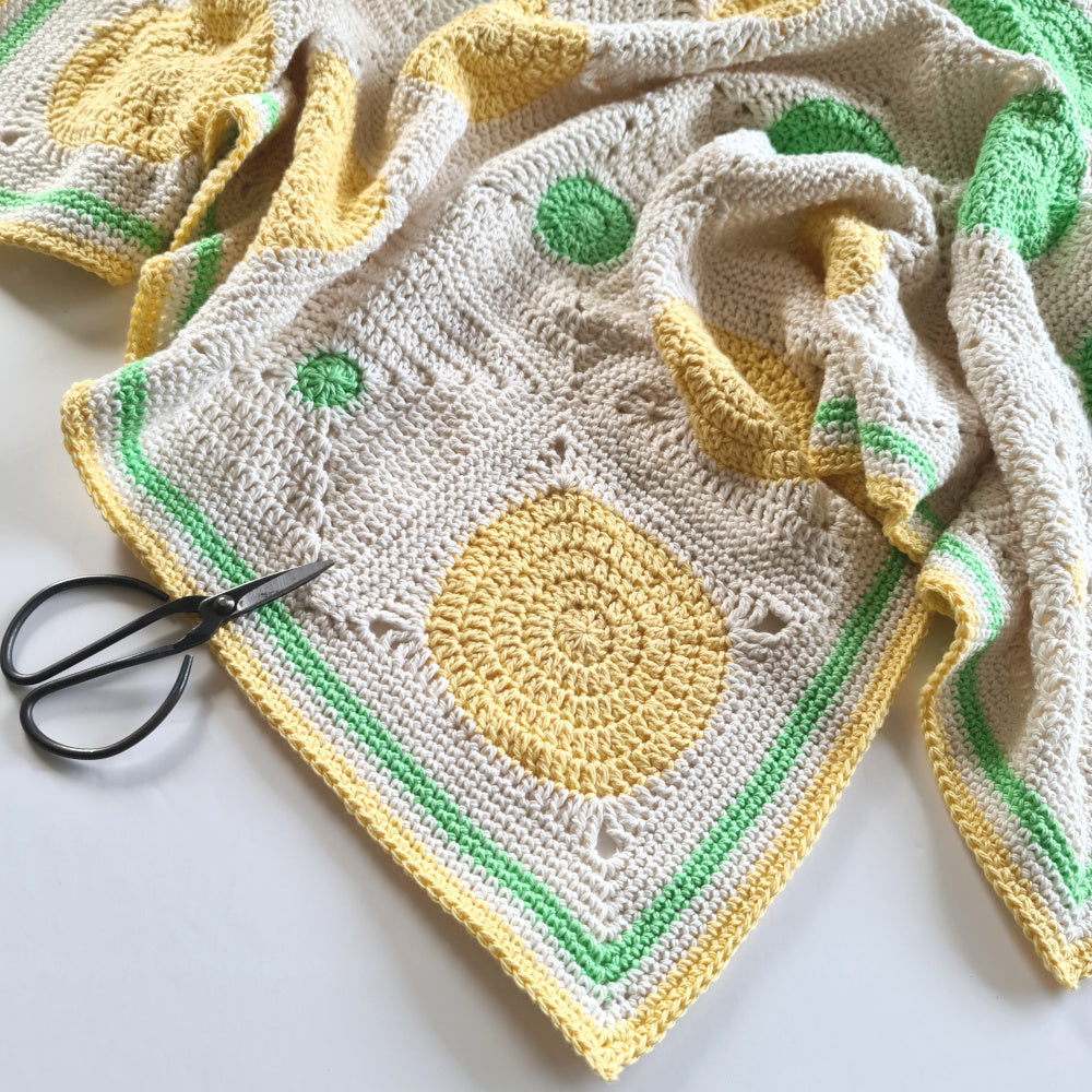 Close up of pale yellow, bright green and parchment Dotty Spotty Blanket highlighting the border at a corner.