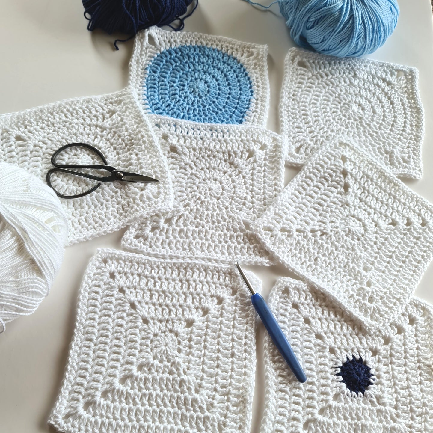 Dotty Spotty granny squares in single colour white with two in blues and white with balls of yarn around them.